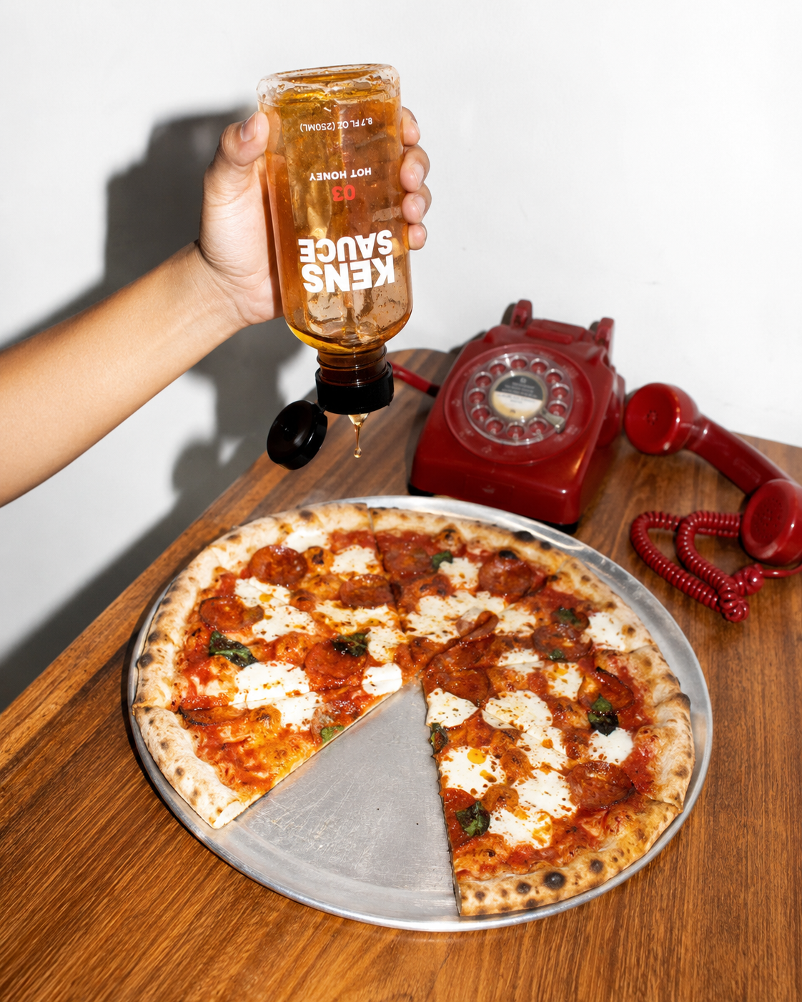 Hot Honey poured over pizza next to a red rotary phone